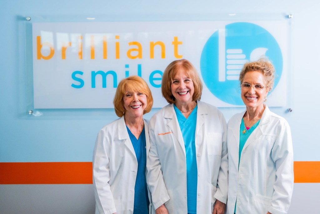 3 Doctor's smiling in front of their dental practice